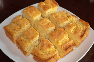 Sliced up corn bread on a white plate on the kitchen table waiting to be eaten.