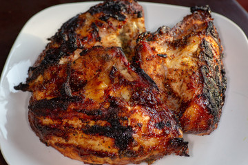 Barbecue chicken breasts fresh off the grill on a white plate on the kitchen table waiting to be eaten.