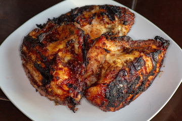 Barbecue chicken breasts fresh off the grill on a white plate on the kitchen table waiting to be eaten.