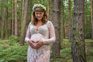Beautiful pregnant woman in white lace dress in forest