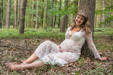 Fototapeta na wymiar Beautiful pregnant woman in white lace dress in forest