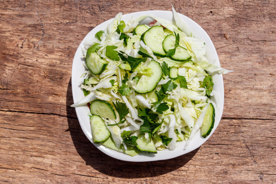 Spring vegan salad with cabbage, cucumber, green onion and parsley on wooden table. Top view
