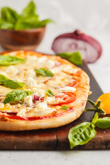 Oval homemade pizza with feta cheese, tomatoes and basil on a wooden board.
