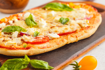 Oval homemade pizza with feta cheese, tomatoes and basil on a wooden board.