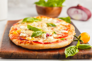 Oval homemade pizza with feta cheese, tomatoes and basil on a wooden board.