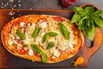Oval homemade pizza with feta cheese, tomatoes and basil on a wooden board.