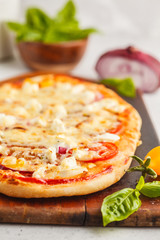 Oval homemade pizza with feta cheese, tomatoes and basil on a wooden board.