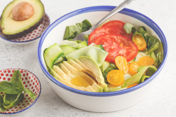 Green zucchini noodles salad with tomatoes, avocado and basil. Healthy vegan zucchini pasta.
