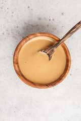 Creamy homemade peanut butter in wooden bowl, top view.