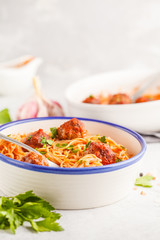 Pasta with meatballs in tomato sauce with parsley and garlic in white dish, white background.