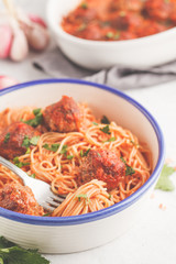 Pasta with meatballs in tomato sauce with parsley and garlic in white dish, white background.