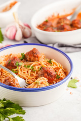Pasta with meatballs in tomato sauce with parsley and garlic in white dish, white background.