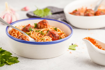 Pasta with meatballs in tomato sauce with parsley and garlic in white dish, white background.