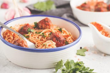 Pasta with meatballs in tomato sauce with parsley and garlic in white dish, white background.