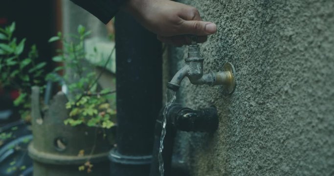 Young man turning on outdoor tap