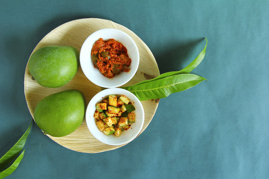 Top view, raw mango, its pieces and mango pickle isolated on green background