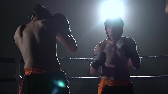 Two guys in helmets and boxing gloves to fight in the ring . Slow motion