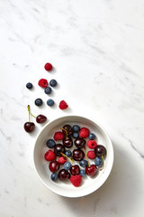 Sweet fresh blueberry, cherry, raspberry on a white plate on gray background with place for text. Top view