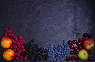 Various fresh summer berries. Mix of fruits and berries on black background. Fruit banner. Selection of healthy vegetarian food, detox or diet concept, space for text. Top view, overhead