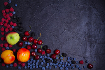 Various fresh summer berries. Mix of fruits and berries on black background. Fruit banner. Selection of healthy vegetarian food, detox or diet concept, space for text. Top view, overhead