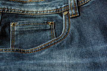 Close-up of a piece of blue jeans with orange stitches. Pocket with rivets close-up.