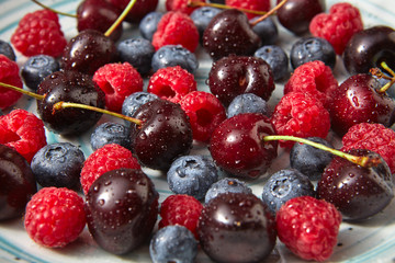 Close-up of summer organic berries - cherry, raspberry, blueberries in water droplets in the blue plate.