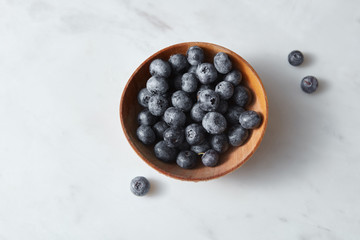 Organic freshly picked blueberry in a wooden bowl on a white kitcen table. Copy space.