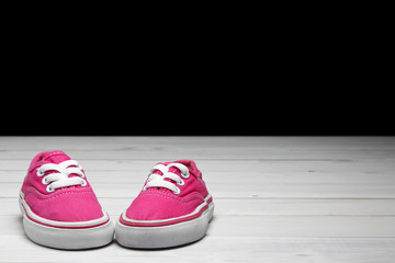 old secondhand pink canvas shoes or sneakers for kid or child and baby foot on vintage white wood floor or table and black wall front view for fashion with space and clipping path on black background
