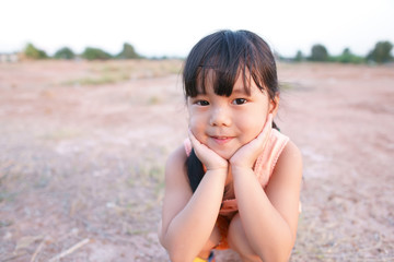 Asian children cute or kid girl smile with poor and happy fun because come back home to country and wear traditional top or sleeveless shirt sit on arid soil for agriculture at home