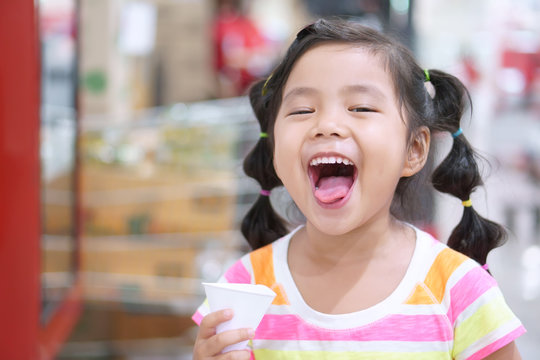 Asian Children Cute Or Kid Girl Thirsty And Drinking Cold Water In White Paper Cone Cup For Healthy And Open Mouth With Tongue And Make Refreshing Face In Department Store Or Super Market