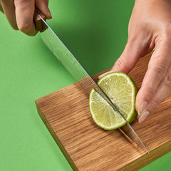 A girl cut a half of green ripe lime to slices on a wooden board on a green background. A sharp...