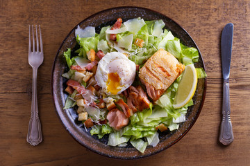 Salmon caesar salad. Crispy pan fried salmon fillet, bacon, poached egg, lettuce and croutons dressed with parmesan cheese. View from above, top studio shot