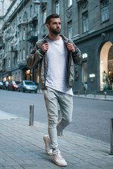 Handsome and casual. Full length of handsome young man adjusting his jacket while standing outdoors