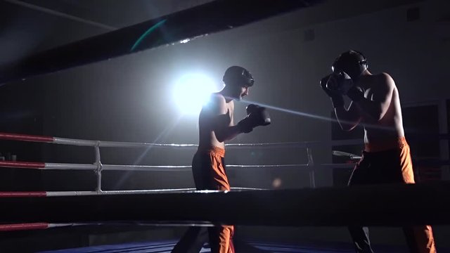 Two guys in the ring fight in the dark . Slow motion