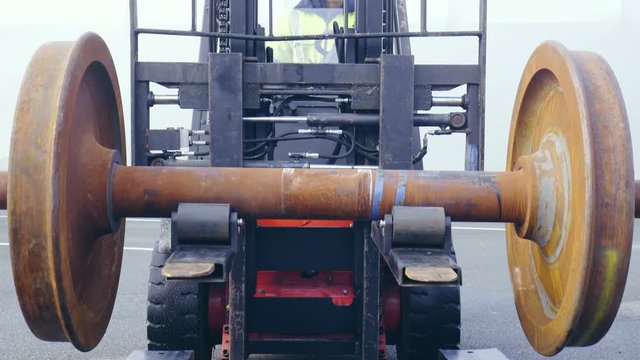 Lifting train wheelbase from an iron pallet with forklift 4K. Wide view of heavy iron wheelbases in focus with a forklift in background lifting them.