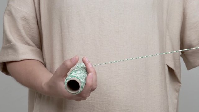 A close-up of woman's hands holding a roll of stripy rope. She pulls the rope and unwinds it, then she winds it back.