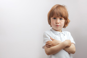 little naughty boy standing with folded arms looking at the cmaer on the isolated white background....