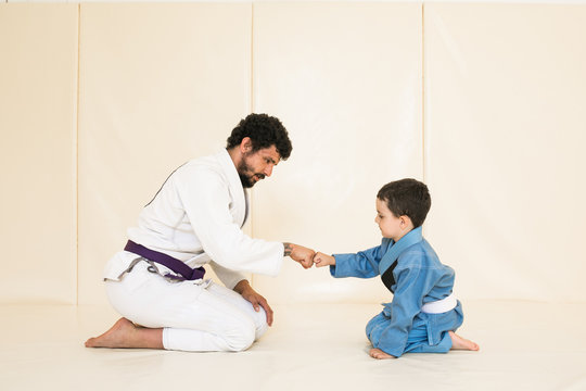 Male karate instructor training little child in dojo or jiu-jitsu at gym at tatami. Trainer teaches kid the basics of fighting for self-defense