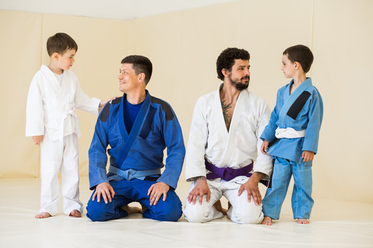 Male karate instructors training little children boys in dojo or jiu-jitsu at gym at tatami. Trainer teaches kid the basics of fighting for self-defense. Group of man and kids in sambo training