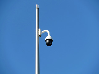 Outdoor surveillance video camera on a pole isolated on clear blue sky. Cctv camera, concept for...