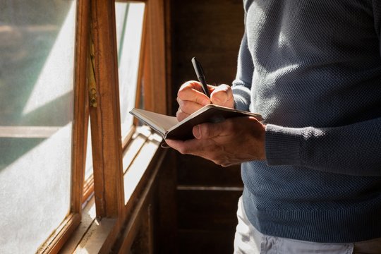Midsection of man writing in diary indoors