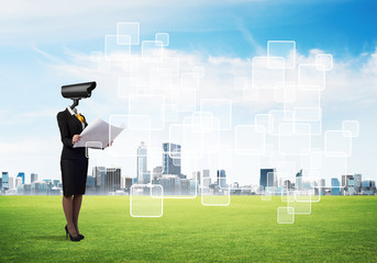 Camera headed woman standing on green grass against modern cityscape