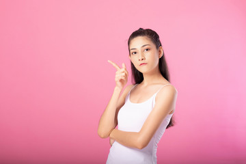 Portrait of a smiling attractive woman in white tanktop outfit with thinking pose while standing and smiling at camera isolated over pink background.