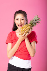 Attractive happy young woman holding fresh pineapple with a smile. Isolated over pink background. Summer lifestyle concept.