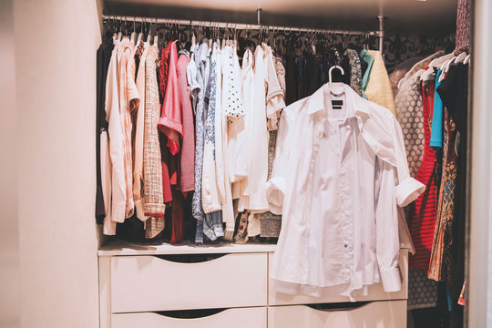 Woman many clothes. Colorful clothes hanging in wardrobe. White men's shirt in women's wardrobe.