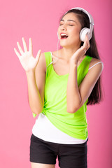 Portrait of a happy attractive woman in summer outfit listening  and dancing to music with her headphones isolated over pink background.