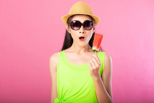 Portrait Of A Happy Attractive Woman In Summer Green Outfit With Hat And Sunglasses Holding Fresh Water Melon On Stick Looking Surprise Isolated Over Pink Background. Summer Vibe Concept.