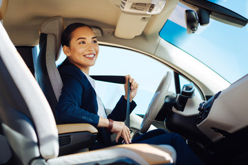 In the car. Happy positive woman smiling while fastening the seatbelt