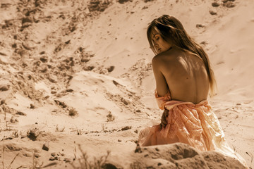 Sexy young girl sits on a sand in a desert