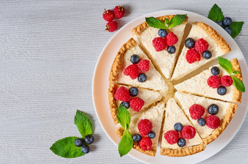 Sliced cheesecake with fresh berries on the white plate - healthy organic dessert. Classic New York cheese cake decorated with blueberries, raspberries and mint. Top view with copy space for text